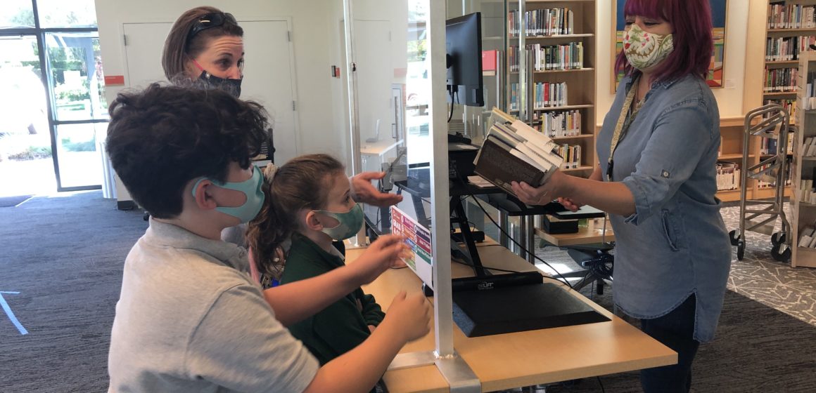 Terra Vitarelli and her children, Luca and Michaela, pick up books placed on hold at the Mission Branch Library in Santa Clara. Photo by Lorraine Gabbert.