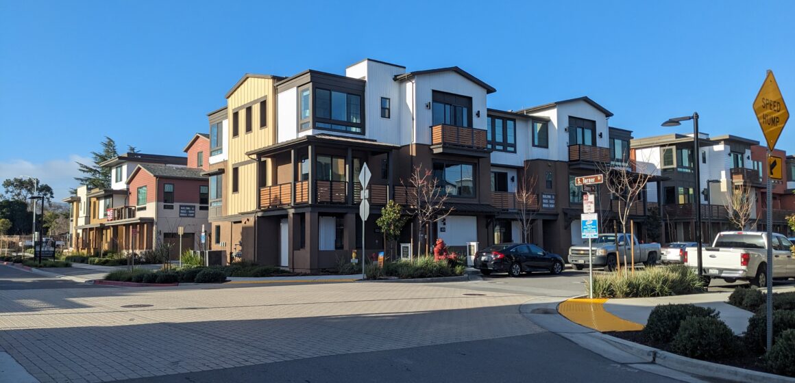 Two story modern homes along a paved street with a blue sky.