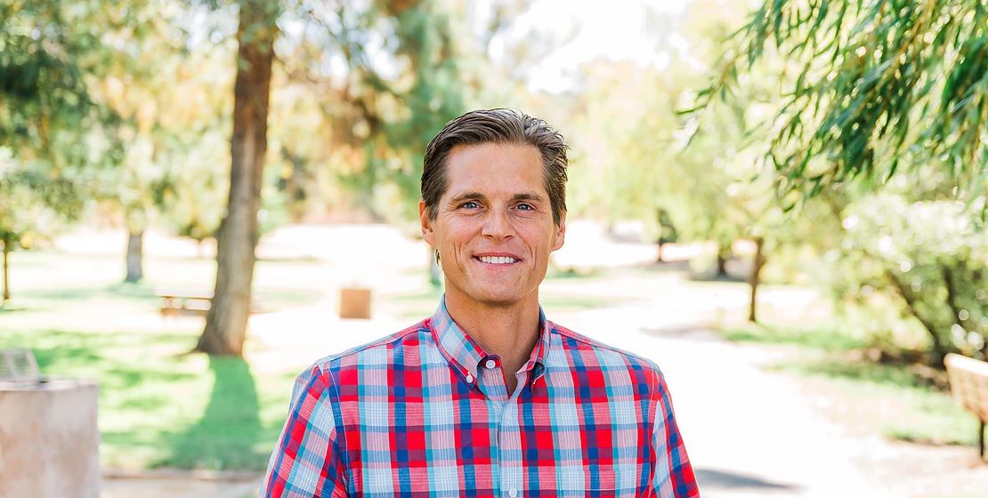 A man stands outside with trees in the background