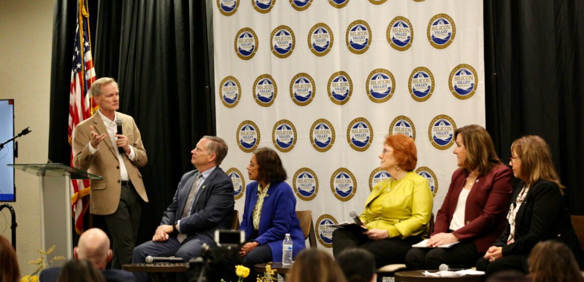 A man with a microphone speaks to a panel of people seated in chairs