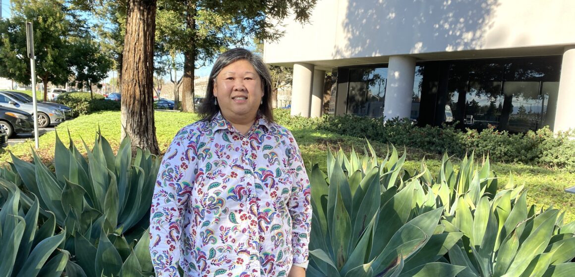 Woman (Buu Thai) standing in front of foliage and building