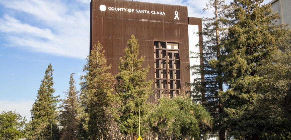 The Santa Clara County Government Center, with trees and cars in a parking lot in the foreground