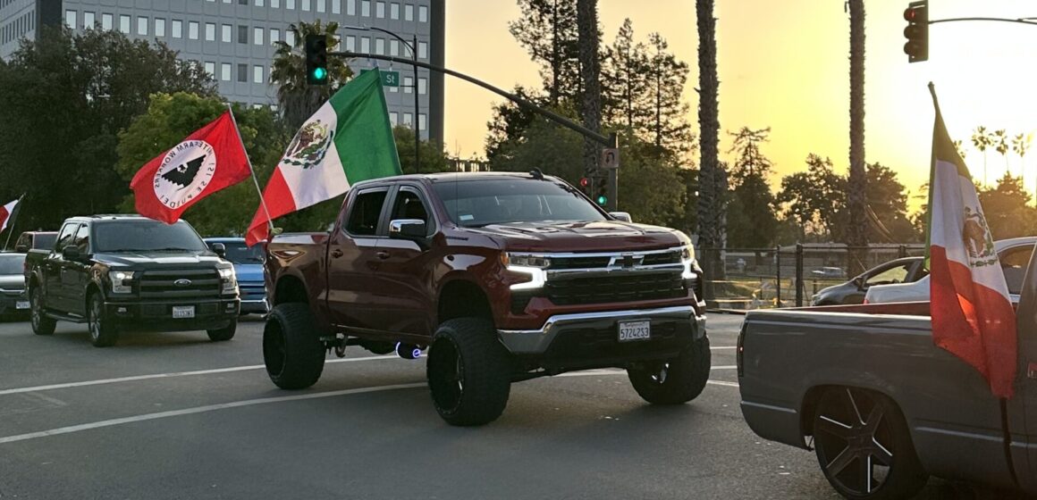 A line of trucks driving down the street carrying the Mexican flag