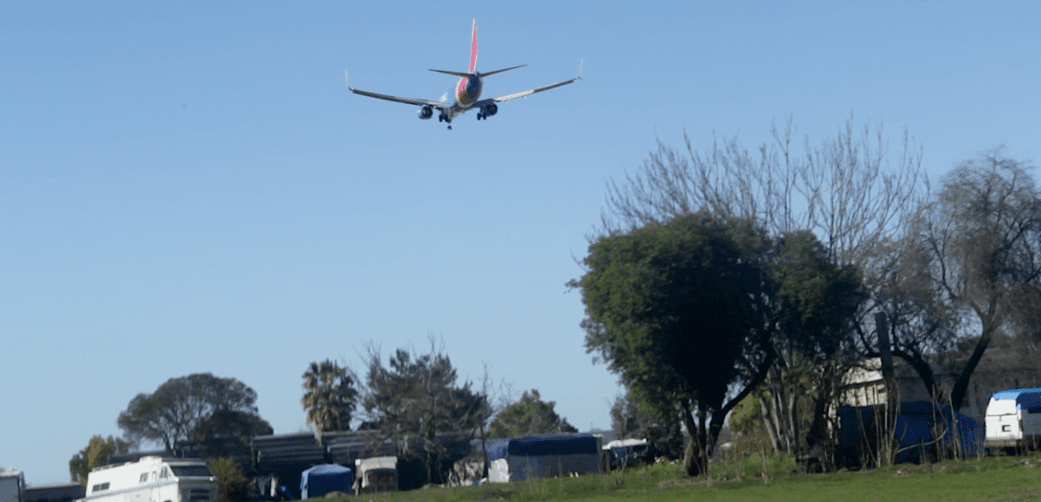 A plane flies over homeless camps on parkland in San Jose