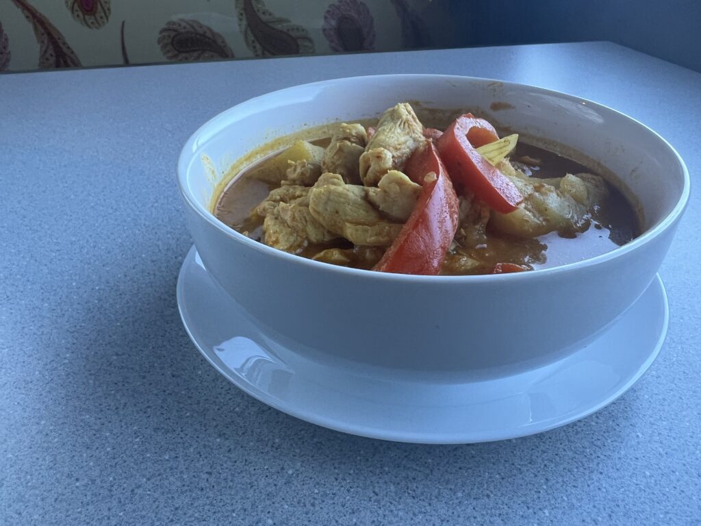 A bowl of orange curry with chicken, bell peppers and potato.