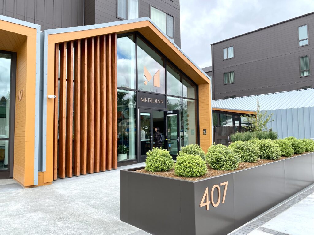 Exterior of building with floor to ceiling glass entrance and name "Meridian" over the doorway, and address number 407 on a planter in front of entrance