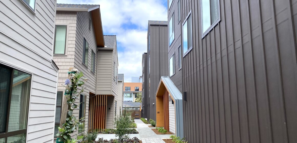 Stone walkway between slat-walled townhomes and slat-walled apartment building