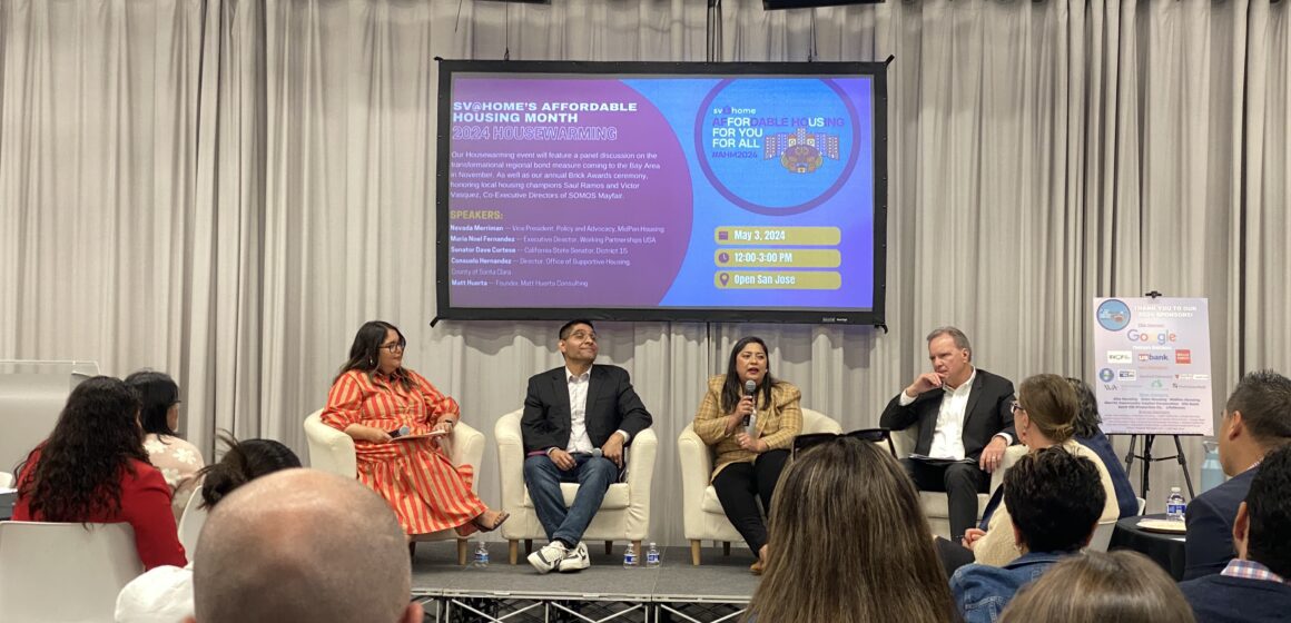 Four people sitting on arm chairs on a raised stage in front of a projected banner introducing "SV@Home's affordable housing month 2024 Housewarming" event