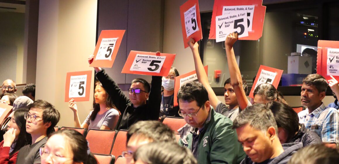 A group of people hold up signs supporting map 5 in a high school auditorium