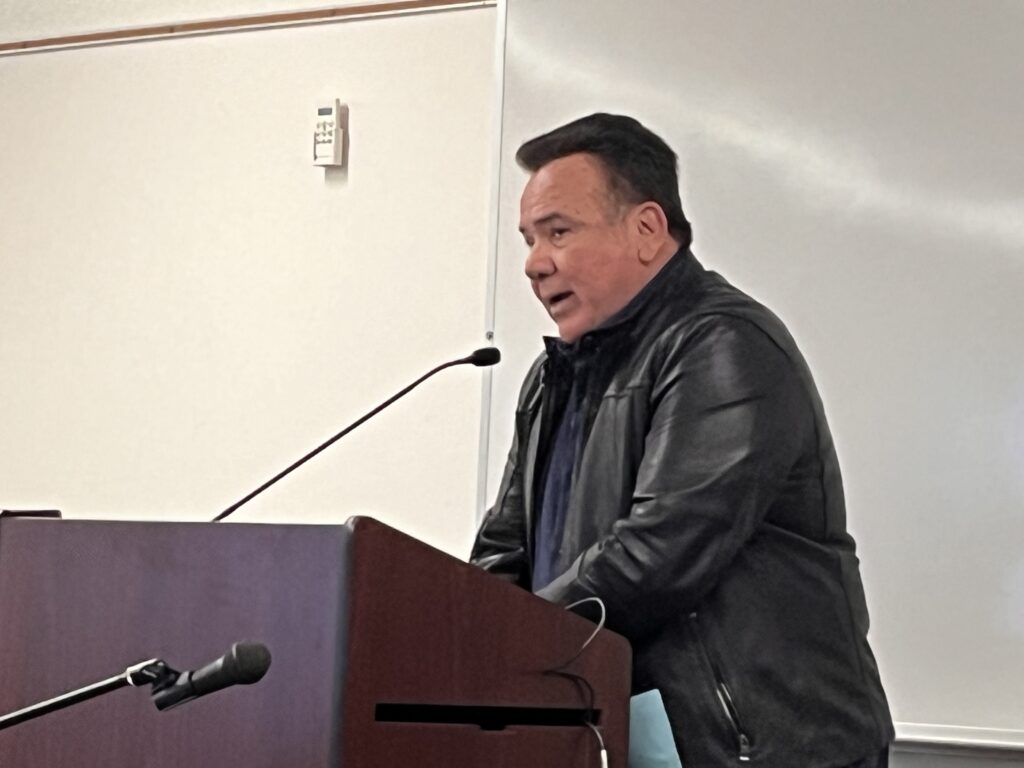 A man stands speaking into a microphone at a podium.