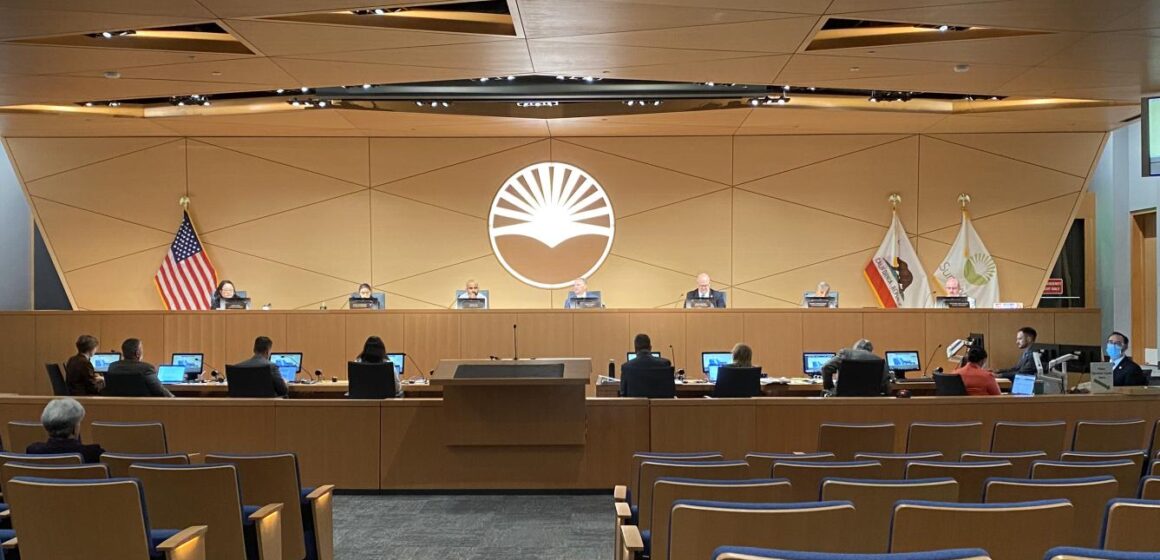 Full Sunnyvale city council seated behind the chamber dais during a meeting, with city staffers seated below.