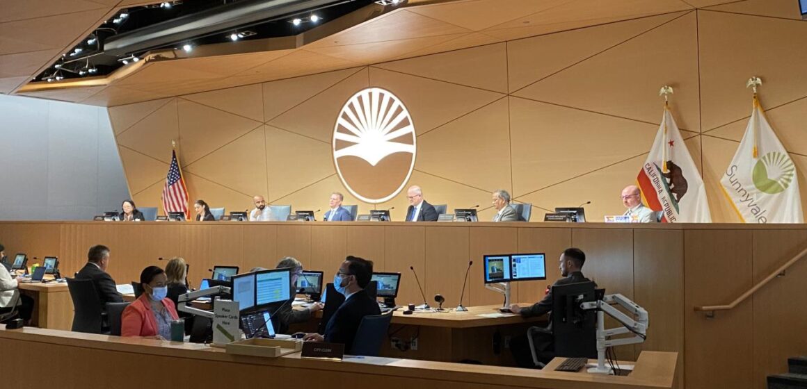 Full Sunnyvale city council seated behind the chamber dais during a meeting, with city staffers seated below.