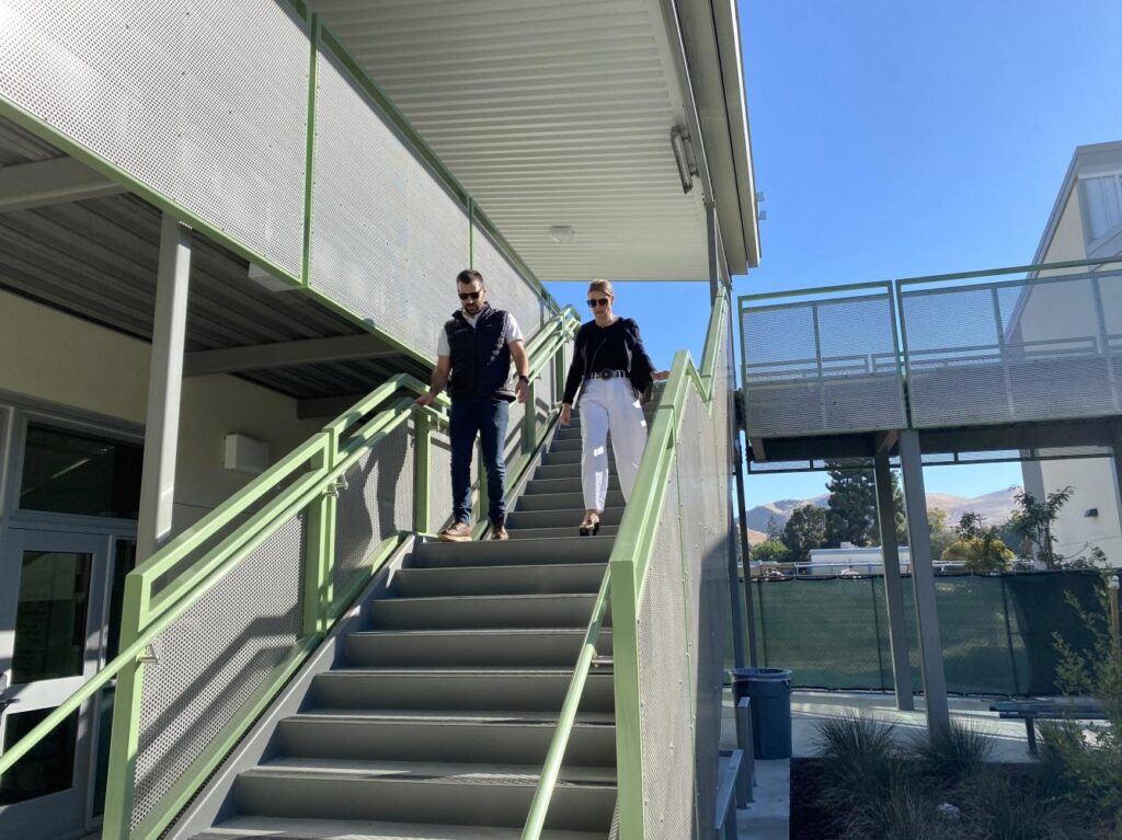 Two people walking down the stairs in the courtyard of a school with construction fencing in the background.