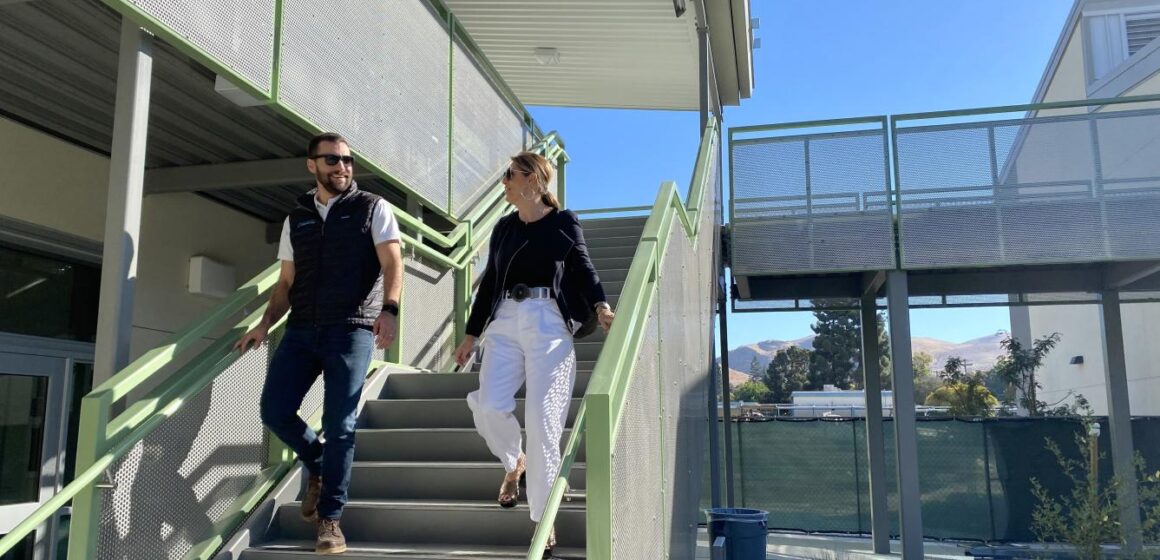 Two people walking down the stairs in the courtyard of a school with construction fencing in the background.