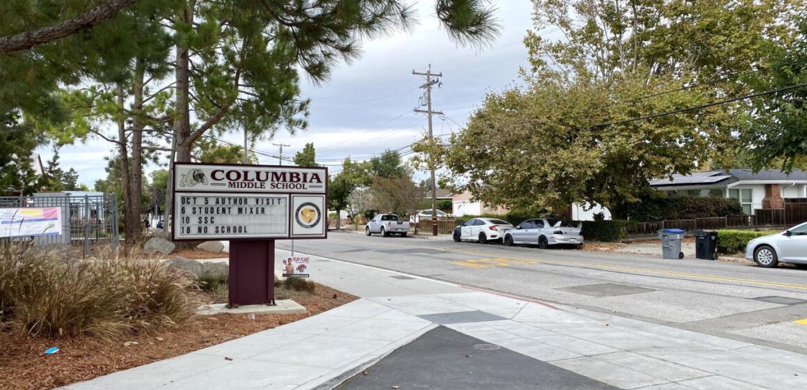 Sign for Columbia Middle School in Sunnyvale, listing dates for school events, showing the school's drop-off driveway and the street in front of the school