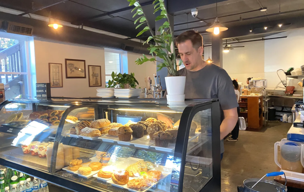 Coffee & More Cafe owner Anton Slade retrieving a pastry for a customer from the cafe's pastry case