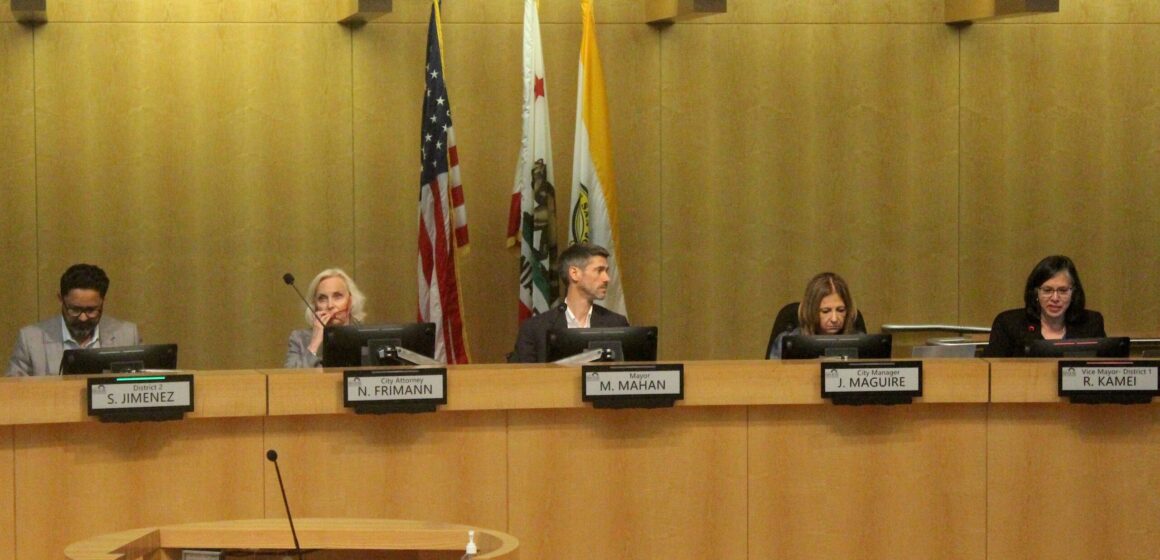 Men and women sitting on a dais at a government meeting