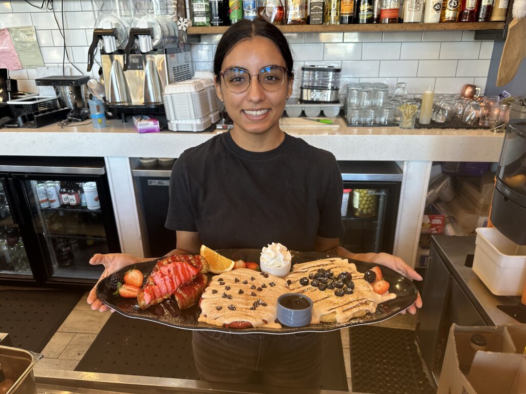 Camila Ruiz holding the Midtown Trio: raspberry stuffed French toast, a red velvet pancake and a blueberry lemon ricotta pancake. Photo by Robert Eliason.