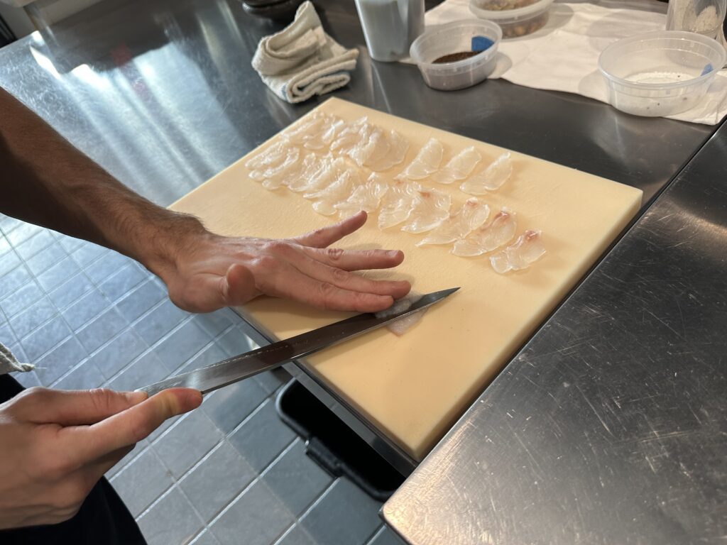 A hand and knife slicing fish on a cutting board.