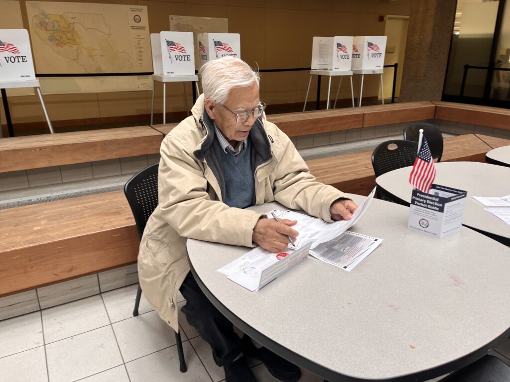 A man sits at a table and fills out his election ballot.