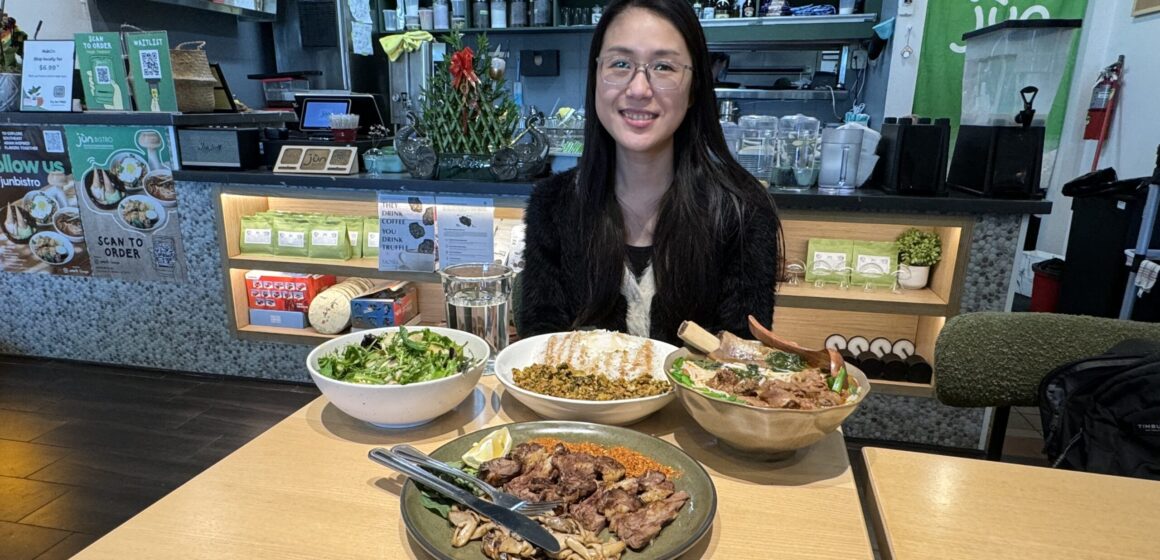 A woman sits inside a Chinese restaurant with several dishes in front of her on the table