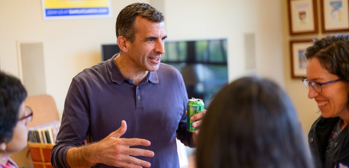 A man stands holding a soft drink while speaking with three women