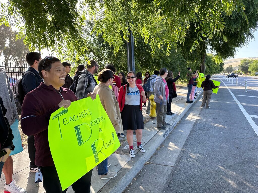 Teachers stand along the curb holding signs asking for better wages