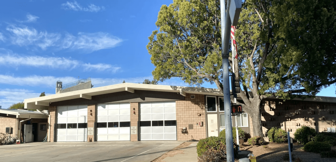 One story fire station building with three large garage doors all closed and big tree in front