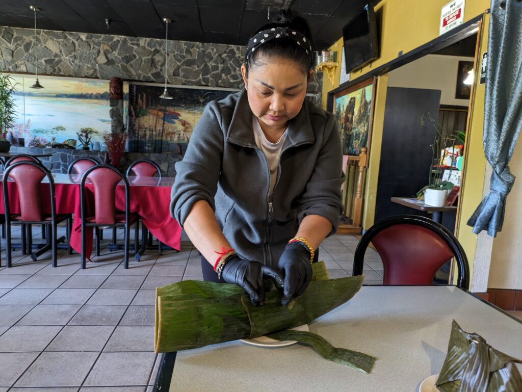 A woman wraps fish in a banana leaf