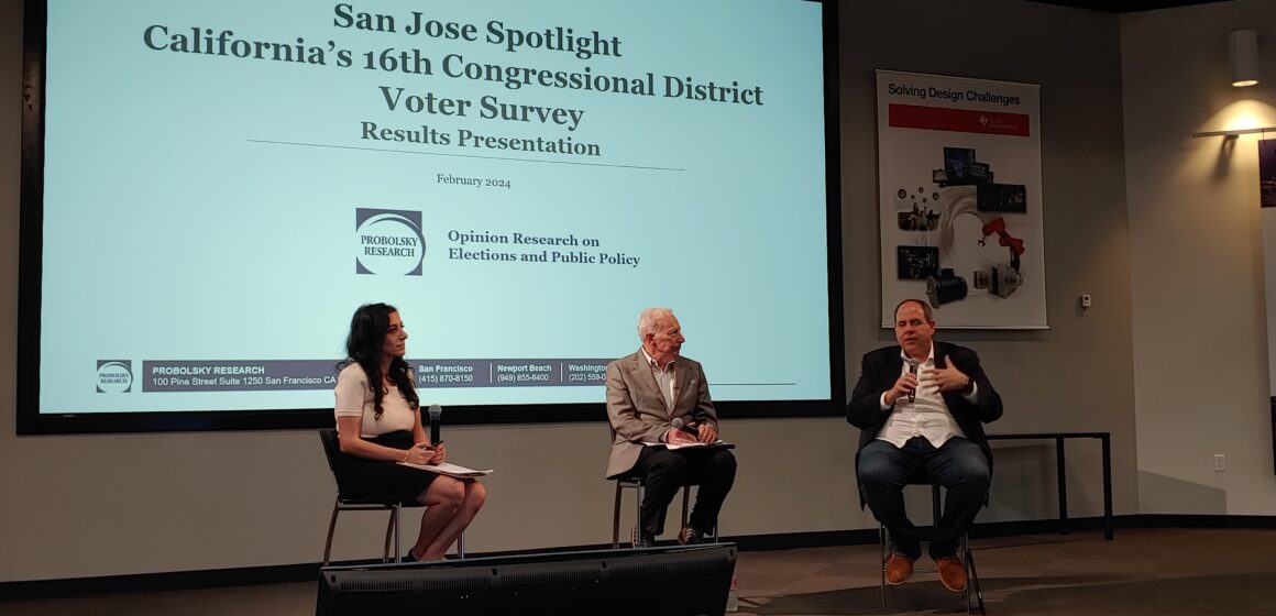 A panel of three people sit in front of a projector screen.