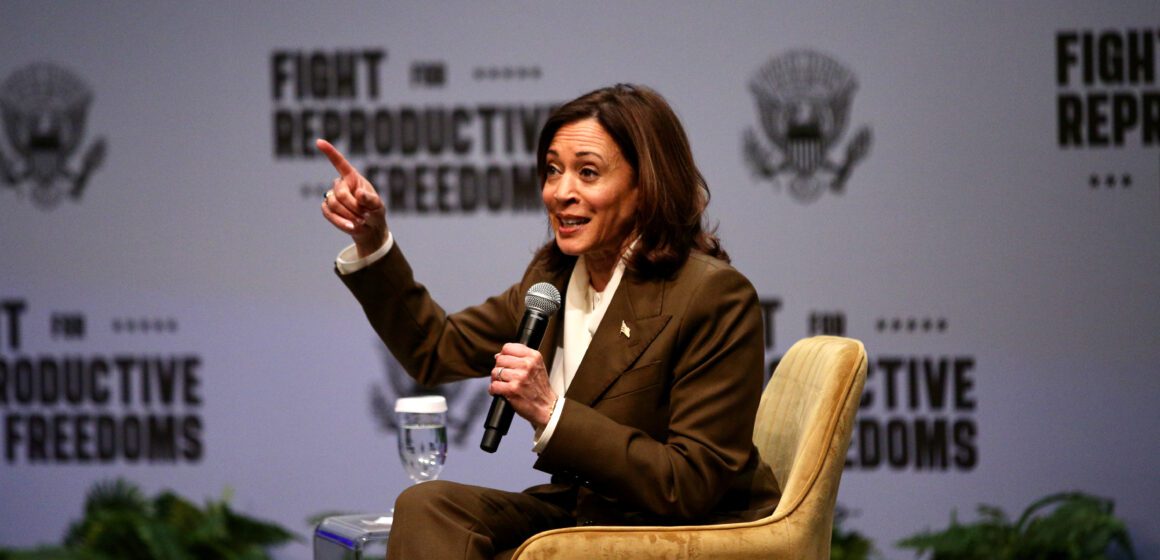 A woman sitting in a chair speaks into a microphone onstage.