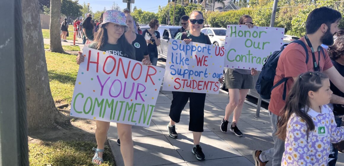 Parents, students and teachers march on the sidewalk holding signs