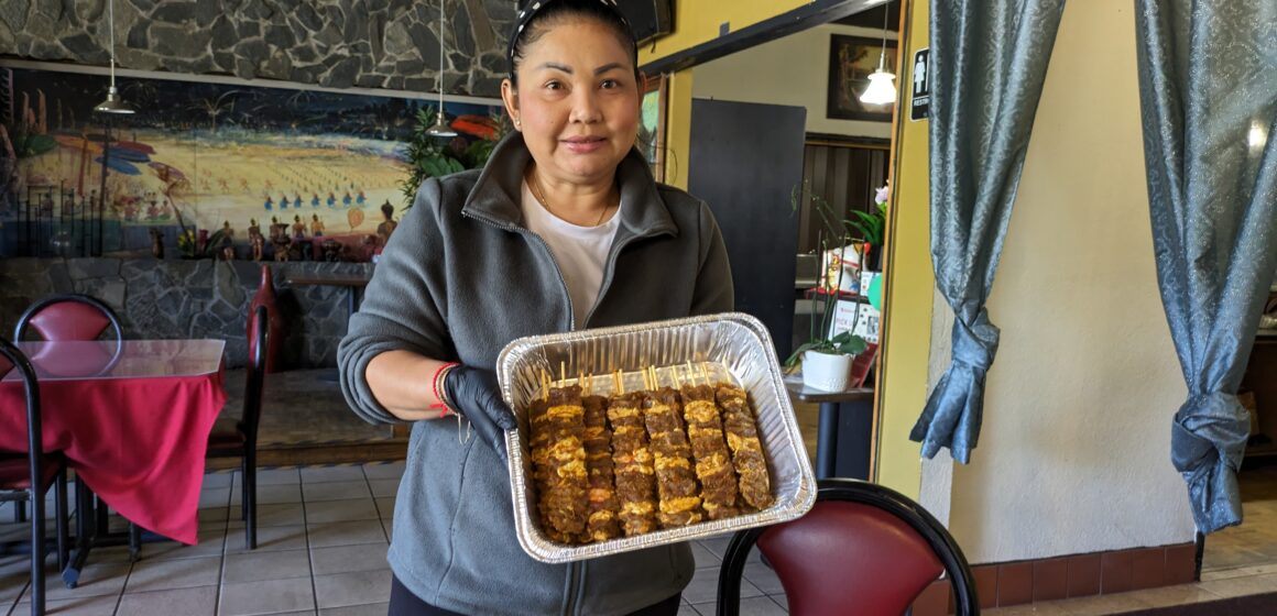 A woman stands in a restaurant holding up a metal tin of uncooked kebab meat