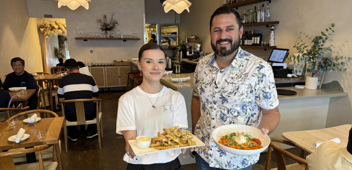 A man and a woman stand facing the camera holding plates of food