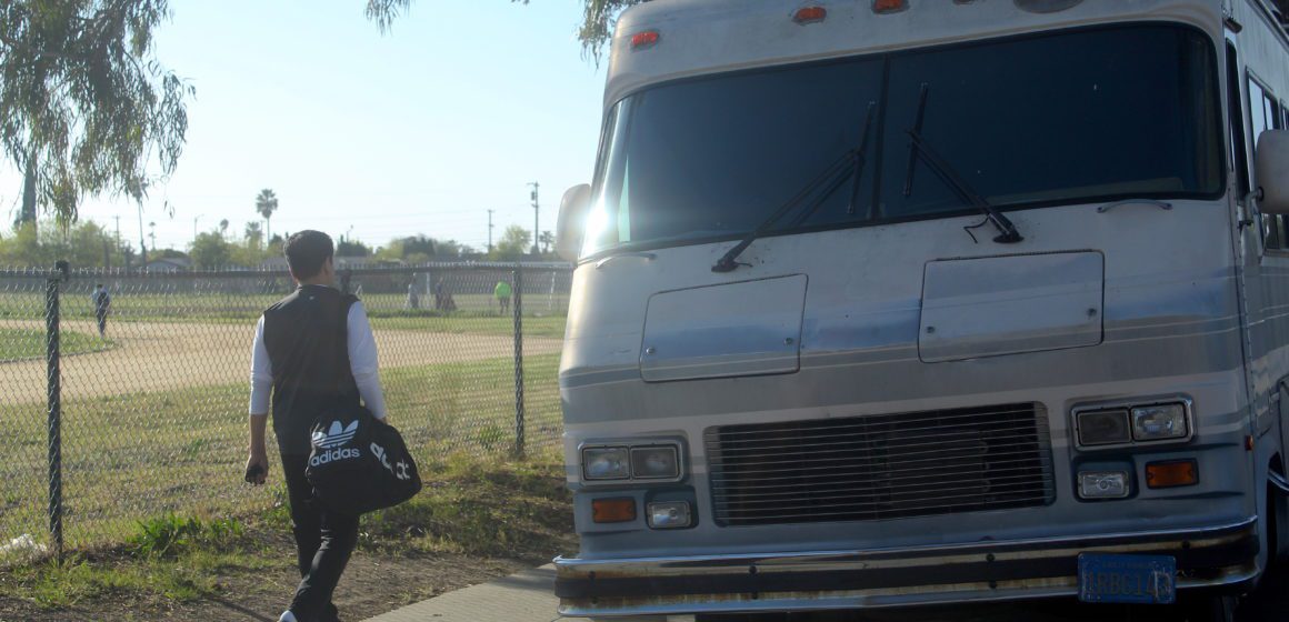 A youth walking past Clyde L. Fischer Middle School in East San Jose where an RV sits in front of the school's track field. Photo by Vicente Vera.