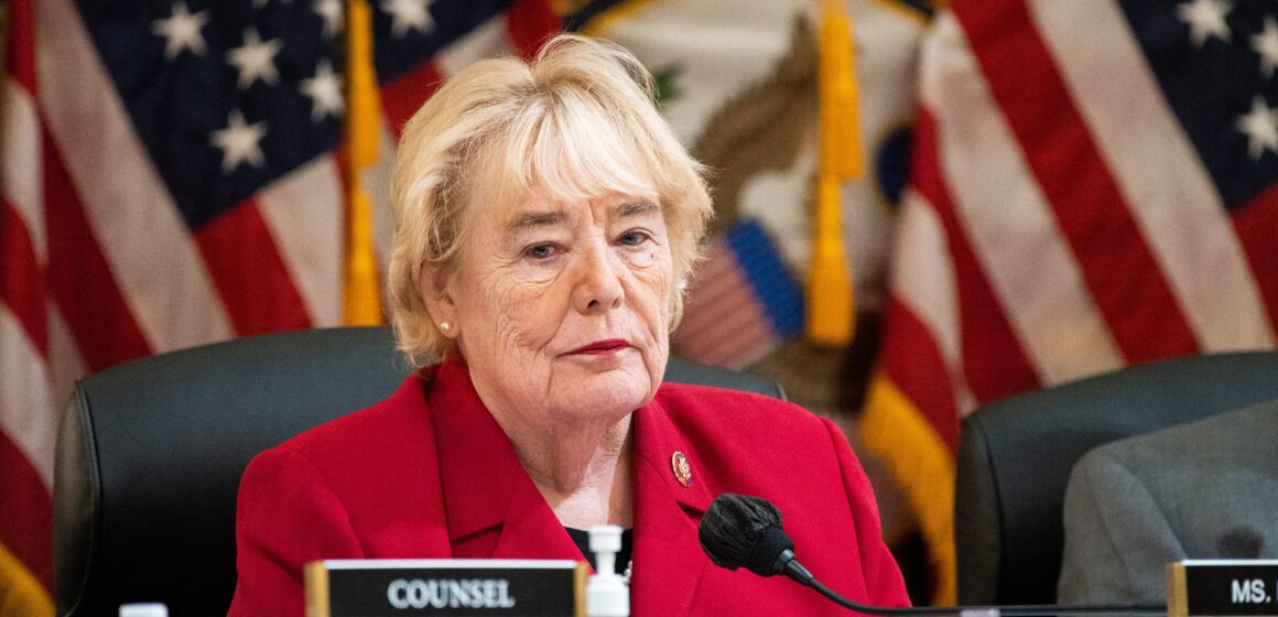 A woman sits at a dais with American flags behind her